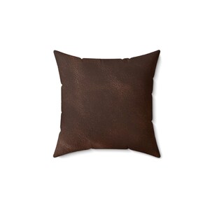 May include: A square throw pillow featuring a dark brown, textured surface that mimics the appearance of leather. The pillow has a simple, clean-edged design with visible stitching along the sides, presenting a uniform and solid color throughout.