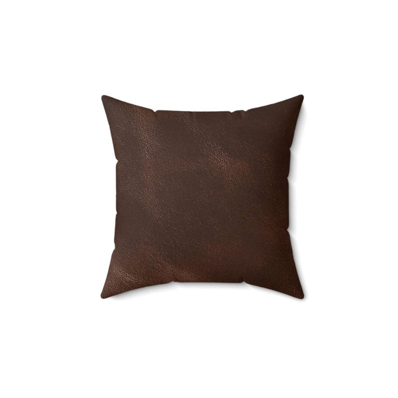 May include: A square throw pillow featuring a dark brown, textured surface that mimics the appearance of leather. The pillow has a simple, clean-edged design with visible stitching along the sides, presenting a uniform and solid color throughout.