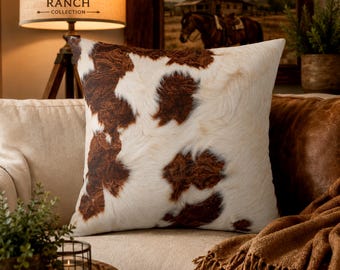 May include: A square throw pillow featuring a realistic cowhide pattern with irregular patches of dark brown and cream white fur. The fabric displays a textured appearance mimicking natural animal hide, presented in a clean, simple square shape.