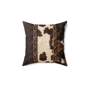 May include: A square throw pillow featuring a central panel of white and brown cowhide print flanked by two vertical strips of brown faux leather with a crisscross stitched pattern, bordered by solid dark brown textured faux leather sides.