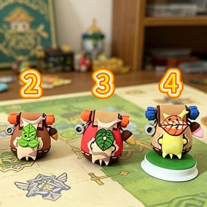 May include: Four colorful, miniature figurines with backpack designs are displayed on a patterned surface. Each figure has a unique color scheme, including red, brown, and blue, with leaf and face details. The figurines are numbered 1 through 4.