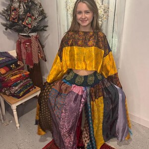 May include: A two-piece outfit featuring a yellow crop top with patterned sleeves and a patchwork design. The wide-leg pants are made of various colorful fabrics. The outfit is worn on a person standing in front of a white wall.