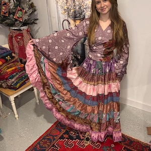 May include: A long, flowing dress with a wrap top and tiered skirt. The dress features a mix of colors including pink, purple, and brown. The sleeves are long and flared. The skirt has multiple layers of fabric with different patterns.