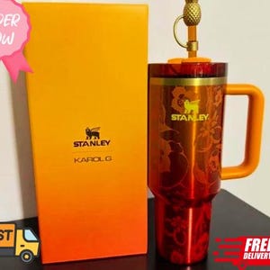 May include: A red and orange Stanley Karol G travel mug with a handle and a pineapple-shaped top. The mug is next to a matching box with the Stanley logo and Karol G's name. The words "Order Now" are in a pink circle.