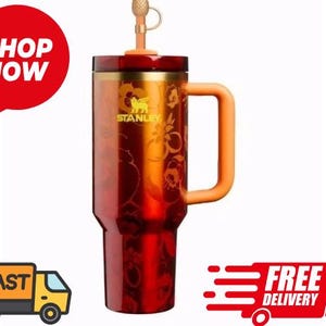 May include: A red and gold Stanley tumbler with a handle and a straw. The tumbler has a floral design and the Stanley logo. The tumbler is designed to keep drinks hot or cold. The tumbler is approximately 9 inches tall.