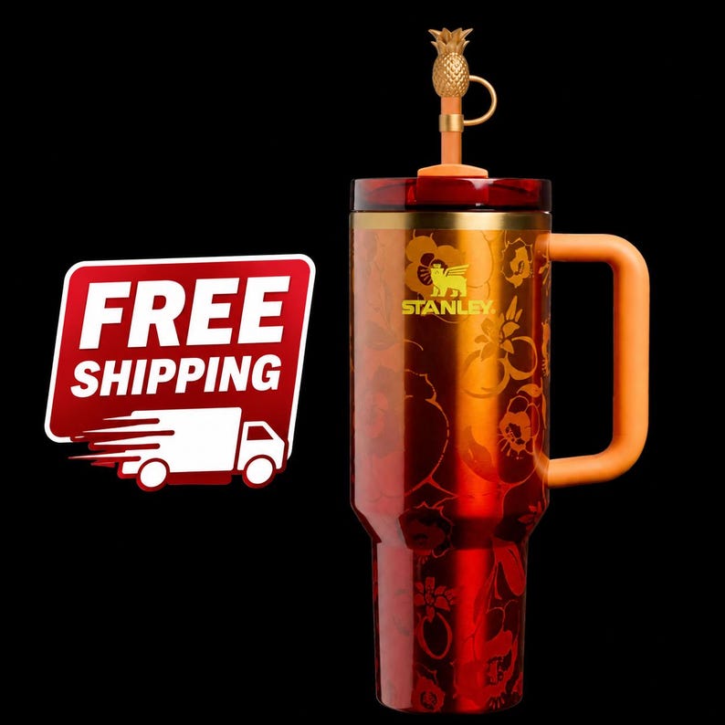 May include: A red and orange Stanley travel mug with a floral design and a gold pineapple-shaped lid. The mug has an orange handle and the Stanley logo. The mug is designed for hot or cold beverages.