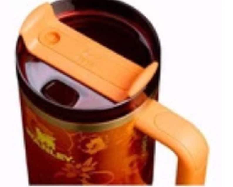 May include: A stainless steel travel mug with an orange handle and lid. The mug has a floral design and the word "STANLEY" in gold lettering. The interior of the mug is dark brown.