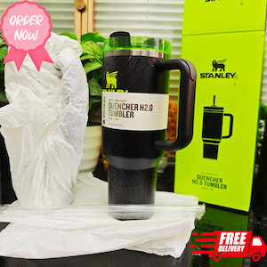 Pode incluir: Caneca Stanley Quencher H2.0 preta com tampa e al&ccedil;a verdes. A caneca tem uma superf&iacute;cie texturizada e um r&oacute;tulo branco com o texto "QUENCHER H2.0 TUMBLER". Uma caixa verde com o logotipo Stanley e a ilustra&ccedil;&atilde;o da caneca est&aacute; no fundo.