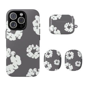 May include: A set of matching phone accessories in a dark gray color, featuring a white floral pattern. The set includes a phone case, an earbud case, and two round pop sockets.