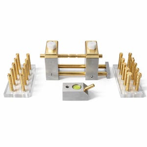 Puede incluir: Un conjunto de herramientas de precisión, que incluye un nivel, varillas de latón y un marco de metal con perillas blancas. Las herramientas están dispuestas sobre una superficie transparente, mostrando su diseño. Los componentes de latón añaden un toque de elegancia.