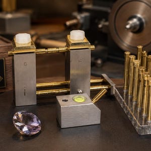 May include: A collection of precision tools, including a level, a gemstone, and a set of gold-colored rods. The tools are arranged on a dark surface, with a wooden box in the background that reads "PRECISION PERFORMANCE PERFECTION".