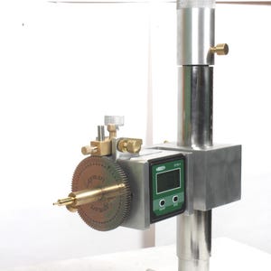 Pu&ograve; includere: Uno strumento di misurazione di precisione dotato di un montante verticale in metallo argentato, uno schermo digitale con accenti verdi e un quadrante circolare color ottone contrassegnato con il testo Lapmart. Include manopole e una punta.