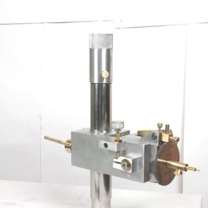 Pu&ograve; includere: Una macchina per sfaccettare in metallo color argento dotata di un montante verticale, un blocco centrale con manopole di regolazione e un braccio orizzontale. Un ingranaggio in ottone con tacche &egrave; fissato lateralmente, dischi metallici sotto.