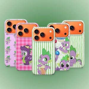Peut inclure: Cinq coques de téléphone avec des motifs colorés représentant un personnage de dessin animé de dragon. Les coques ont des boîtiers d'appareil photo orange et divers motifs, dont du vichy rose, des rayures vertes et des illustrations de personnages.