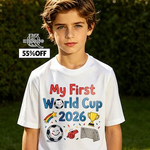 May include: A white t-shirt with the text "My First World Cup 2026" in red and blue. The shirt features soccer-themed graphics, including a soccer ball, trophy, and goal. The shirt is being worn by a young person.