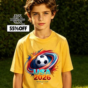 May include: A yellow t-shirt featuring a soccer ball design with the text "USA 2026 World Cup". The shirt also has a graphic of red, blue, and white swirls. The shirt is being worn by a person.