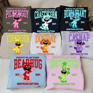 Puede incluir: Colección de sudaderas con personajes de Poppy Playtime. Cada sudadera muestra un nombre de personaje como "Pickypiggy" o "Craftycorn", el año "2024" y la frase "Nightmare Critters". Las sudaderas están en varios colores.