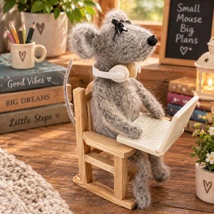 May include: A fuzzy grey needle-felted mouse figurine sitting on a small wooden chair. The mouse wears white headphones around its neck and types on a miniature white laptop. A black chalkboard sign nearby displays the text Small Mouse Big Plans.