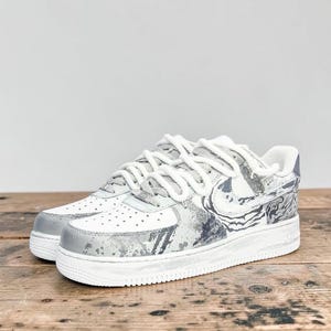May include: Pair of white and gray sneakers with a marble-like design. The shoes have white laces, a white sole, and gray accents on the toe and heel. The Nike swoosh is visible on the side.