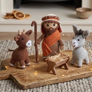 May include: Crocheted nativity scene featuring a shepherd with a staff, a donkey, and a calf. The figures are brown, gray, and white, with orange and tan accents. A wooden manger with hay sits in front of the shepherd.