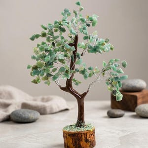 Könnte beinhalten: Ein dekorativer Edelsteinbaum mit braunem Stamm und Ästen aus Silberdraht. Die Blätter sind kleine, hellgrüne Edelsteine. Der Baum steht auf einem Holzsockel mit grünen Akzenten.