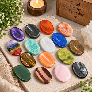 Può includere: Una collezione di sedici pietre preziose levigate di forma ovale e liscia in vari colori, tra cui viola, nero, arancione, blu, verde, bianco, occhio di tigre giallo-marrone, rosa e una pietra a strisce multicolore su una superficie di pietra.