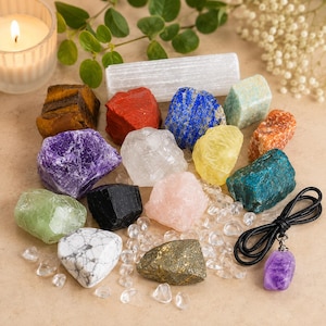 Może przedstawiać: Kolekcja surowych, wielokolorowych kamieni mineralnych, w tym tygrysie oko, czerwony jaspis, lapis lazuli, ametyst, kwarc przezroczysty, cytryn, czarny turmalin, kwarc różowy, piryt i biały howlit, a także różdżka selenitowa i wisiorek z ametystem.