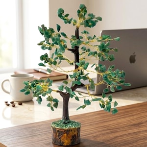 Könnte beinhalten: Eine dekorative Baumskulptur mit einem dunkelbraunen Stamm und Ästen, verziert mit grünen Edelsteinblättern und Golddraht. Der Baum steht in einem Holzsockel und schafft eine natürliche Ästhetik. Die Skulptur ist etwa 20 cm hoch.