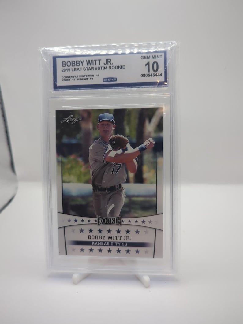May include: A baseball card featuring Bobby Witt Jr. in a Kansas City Royals uniform. The card is graded GEM MINT 10 and is a 2019 Leaf Star #ST04 Rookie card. The card is encased in a protective holder.