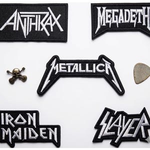 May include: A collection of black and white patches featuring heavy metal band logos, including Anthrax, Megadeth, Metallica, Iron Maiden, and Slayer. Also included are a guitar pick and a skull-and-crossbones pin.