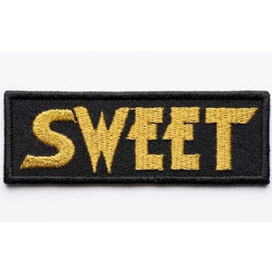 Pode incluir: Um patch retangular preto com a palavra "SWEET" bordada em fio dourado. O patch tem um design simples e arrojado, com as letras em uma fonte estilizada. Ele é projetado para ser costurado ou passado a ferro em roupas ou acessórios.