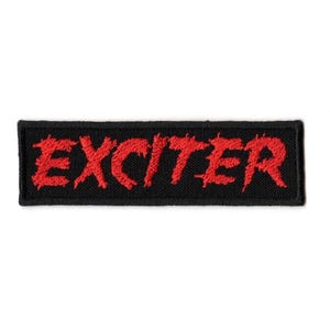 May include: A black rectangular patch featuring the word "EXCITER" in red, embroidered lettering. The patch has a woven texture, suitable for sewing onto garments or accessories.