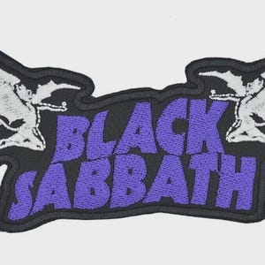May include: Embroidered patch featuring the words "BLACK SABBATH" in purple, with a black border. The design includes two white figures with wings on either side of the text, creating a symmetrical layout.