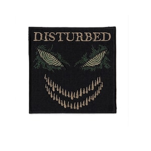 May include: Black square patch with the word "DISTURBED" embroidered in tan thread. The patch features a stylized face with green and tan eyes and a tan toothy grin.