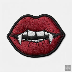 May include: An embroidered patch shaped like a pair of red lips with white teeth and sharp fangs. The design features detailed stitching in shades of red, white, and black, with a thick black border outlining the entire shape of the mouth.