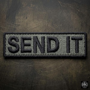 Può includere: Una toppa rettangolare con le parole "SEND IT" ricamate in filo nero su sfondo verde. La toppa ha un bordo nero ed è progettata per essere cucita o attaccata a vestiti o attrezzature.
