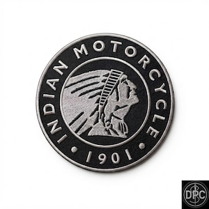 May include: A circular embroidered patch featuring a black background with a silver-toned border. The center displays a silver-toned profile of a person wearing a headdress. The text INDIAN MOTORCYCLE 1901 is stitched in silver around the border.