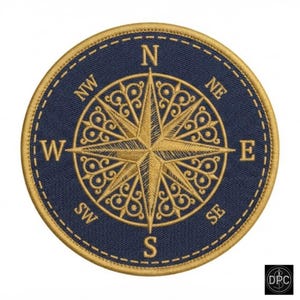 Könnte beinhalten: Ein runder gestickter Aufnäher mit dunkelblauem Hintergrund und einem goldenen Kompassrosen-Design. Der Kompass zeigt die Himmelsrichtungen N, S, O, W, NO, NW, SO und SW in goldener Schrift, umrandet von einer goldenen Stickkante.
