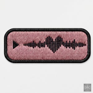 May include: A rectangular embroidered patch with a dusty rose pink background and a black border. The design features a black play button icon on the left and a black sound wave graphic in the center that forms a heart shape in the middle.