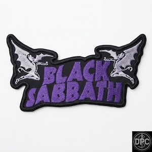May include: An embroidered patch featuring the text BLACK SABBATH in purple thread on a black background. The design includes two light gray winged figures, one on each side of the text, with a black stitched border outlining the entire shape.
