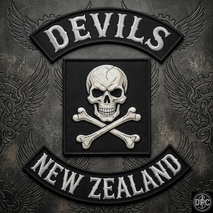 May include: A black embroidered patch set featuring a central square with a white skull and crossbones. An arched top rocker reads DEVILS in white, and an arched bottom rocker reads NEW ZEALAND in white. The design includes stylized wings.