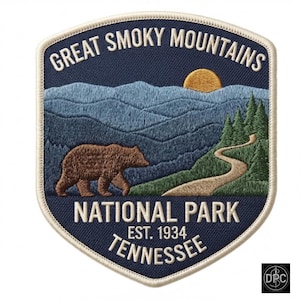 May include: A shield-shaped embroidered patch featuring a dark blue background with the text GREAT SMOKY MOUNTAINS NATIONAL PARK EST. 1934 TENNESSEE. The design shows a brown bear, a winding path, green pine trees, and a yellow sun over blue mountains.