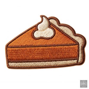 Puede incluir: Un parche bordado con forma de porción de tarta de calabaza. El relleno es de color naranja vibrante, cubierto con una porción de nata montada color crema. La corteza es de color tostado claro y todo el borde está rematado con hilo marrón.