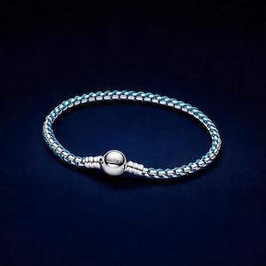 Könnte beinhalten: Ein silberfarbenes Armband mit geflochtenem Design, bei dem eine leuchtend blaue Kordel mit metallischen Gliedern verflochten ist. Das Armband verfügt über einen kugelförmigen Verschluss mit der Gravur PANDORA für einen sicheren Halt.