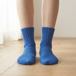 May include: A pair of vibrant blue knit socks featuring a textured, honeycomb-like stitch pattern on the foot and a ribbed cuff design. The socks reach mid-calf and are crafted with a consistent solid blue yarn throughout the entire garment.