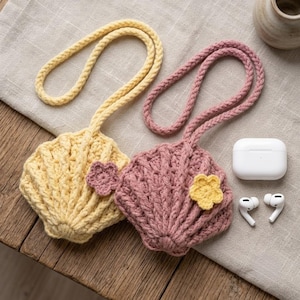 Puede incluir: Dos bolsos de ganchillo con forma de concha, uno en amarillo pálido y otro en rosa empolvado. Cada bolso cuenta con una correa trenzada a juego y una pequeña flor de ganchillo en contraste. Un estuche de carga blanco para auriculares.