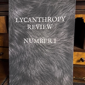 May include: A rectangular book cover with a dark grey and black fur-like texture pattern. The white text printed on the front reads LYCANTHROPY REVIEW NUMBER I in a serif font. The design features a dense, realistic appearance of animal hair.