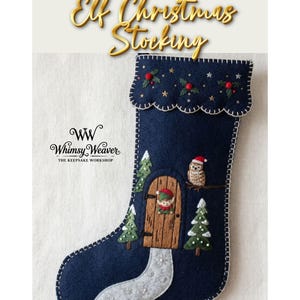 Pode incluir: Uma meia de Natal de feltro azul-escura com detalhes bordados, incluindo uma porta de madeira com um elfo, uma pequena coruja com um gorro vermelho, pinheiros verdes e um caminho nevado. A bainha é decorada com bagas e estrelas.