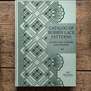 Puede incluir: Un libro titulado "Catálogo de patrones de encaje de bolillos" con una cubierta verde claro y un diseño de encaje verde oscuro. El título del libro está en texto blanco sobre un rectángulo gris. Guía de diseños de encaje clásicos y modernos.