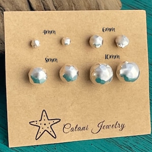 May include: A set of six silver hammered metal earrings in four different sizes: 4mm, 6mm, 8mm, and 10mm. The earrings are displayed on a brown card with the sizes labeled and the text "Catani Jewelry" printed on the bottom.